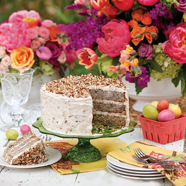 Hummingbird Cake on a green stand surrounded by bright pink, yellow, and purple flowers