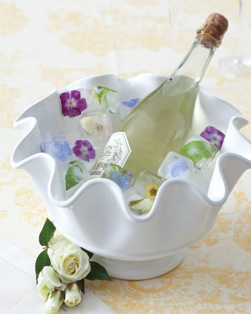 White ruffle-edge bowl holding flower ice cubes and bottle of wine