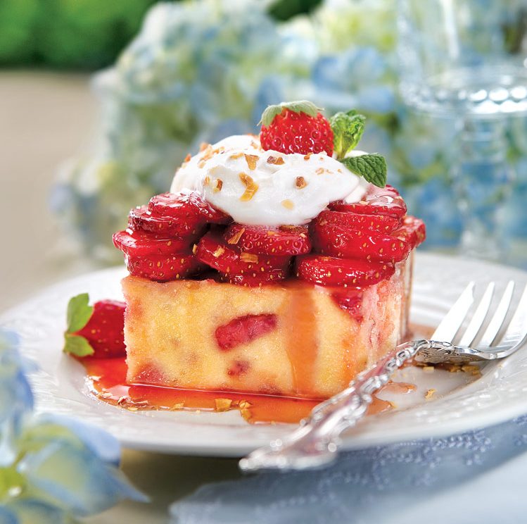 A piece of strawberry shortcake with whipped cream on a white plate and blue linen