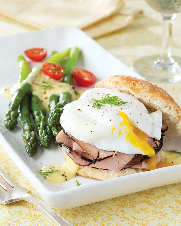Poached egg and ham on an open-faced biscuit sandwich served with asparagus and cherry tomatoes on white platter