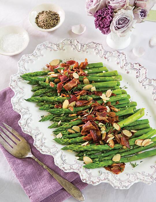 Asparagus topped with bacon and almonds on an ornate white platter