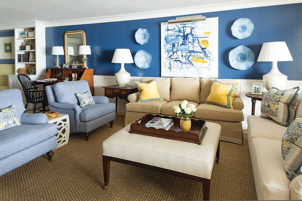 Living area with blue walls, cream sofas, pale blue armchairs, and yellow accent pillows