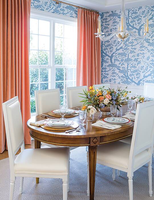 A dining room featuring blue arbor-motif wallpaper and blush draperies