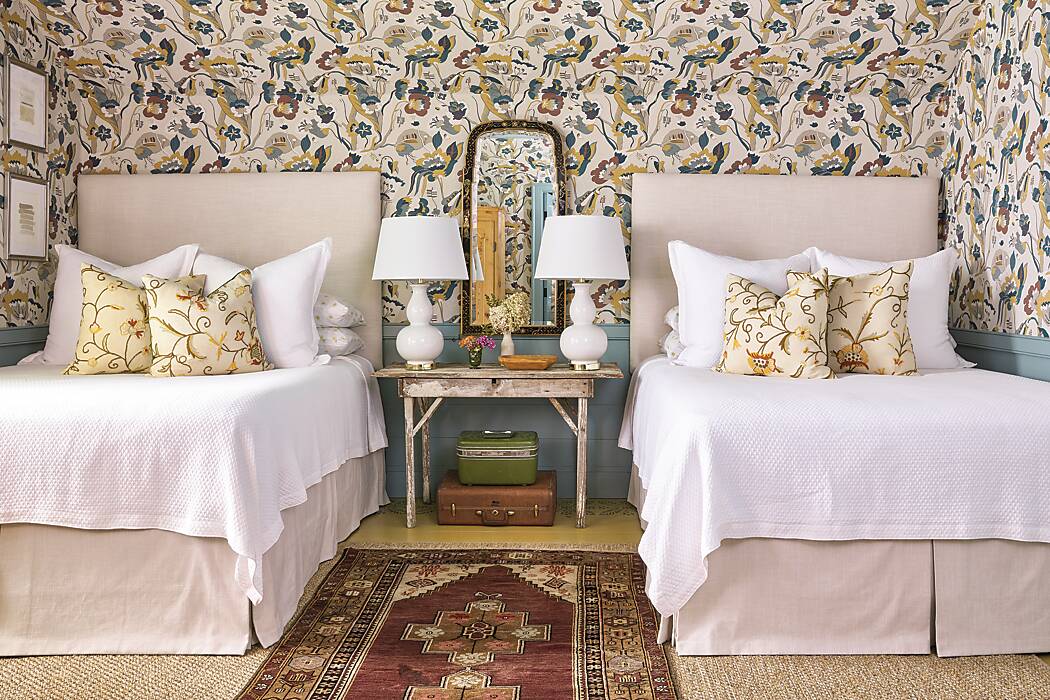 A bedroom with two beds featuring a bold floral wallpaper and blue wood paneling 