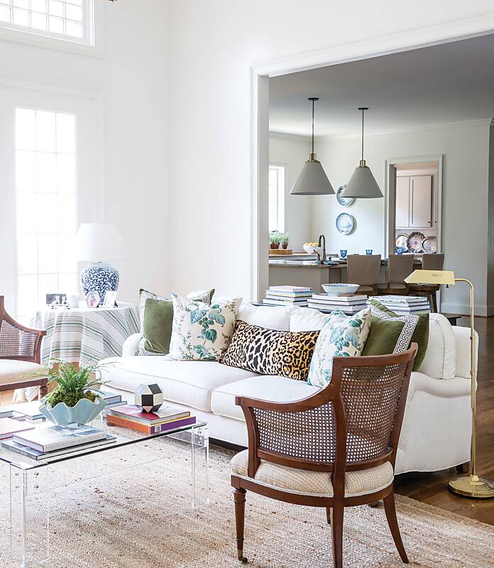 Whitewashed living room with acrylic coffee table, a cane-back chair, and a sofa with mismatched accent pillows