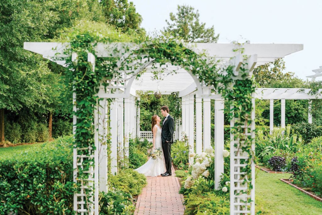 A bride and groom looking at each other beneath a vine-wrapped pergola at The Fearrington House Inn