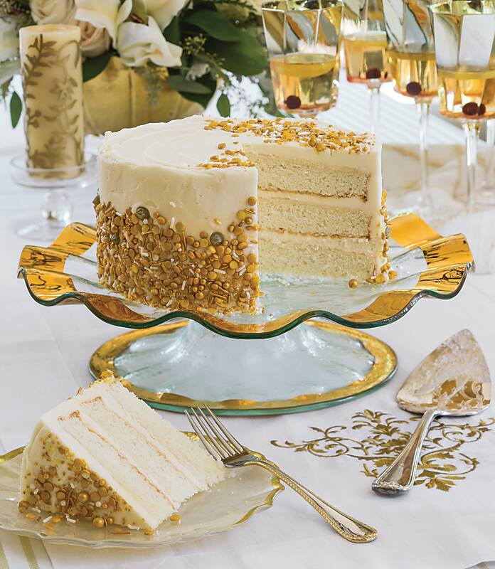 A vanilla layer cake decorated with gold sprinkles on a ruffled cake stand