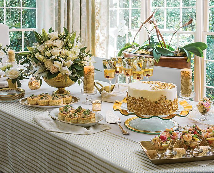 A gold-and-white tabletop set with food, drinks, and flowers for a golden anniversary celebration