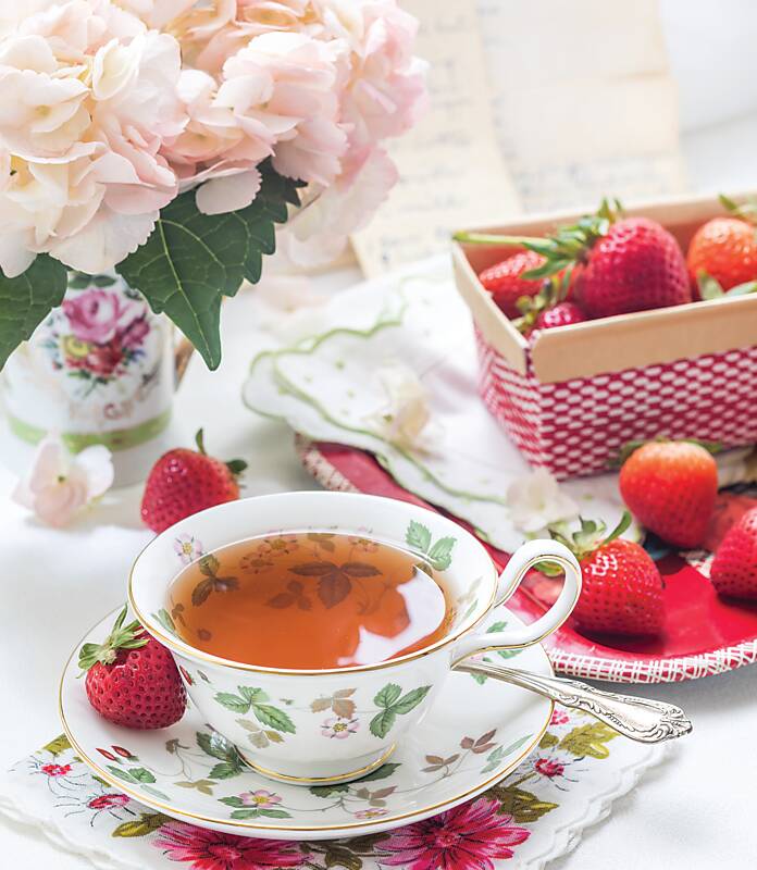 Fine china teacup and saucer surrounded by strawberries and pink flowers