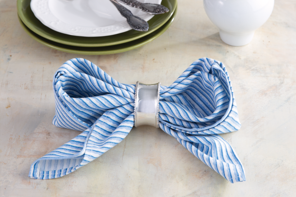 Blue-and-white striped napkin folded into a bow with silver napkin ring