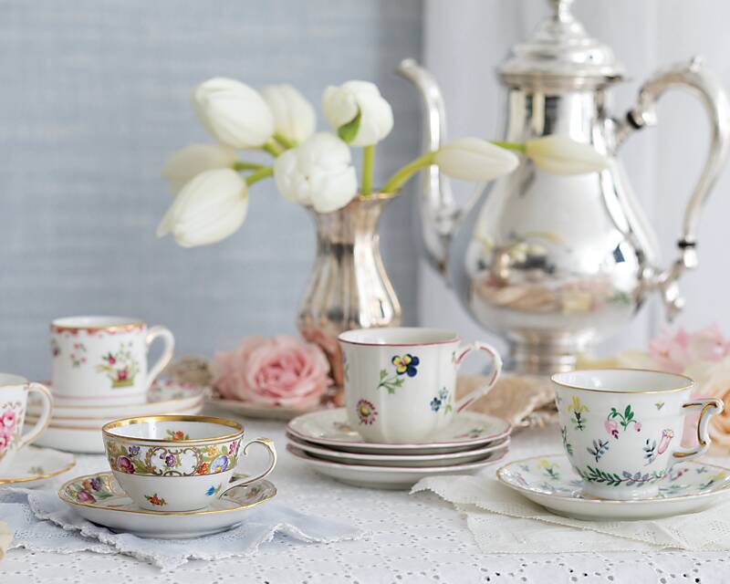Assorted floral demitasse cups and saucers with a silver coffee service in the background