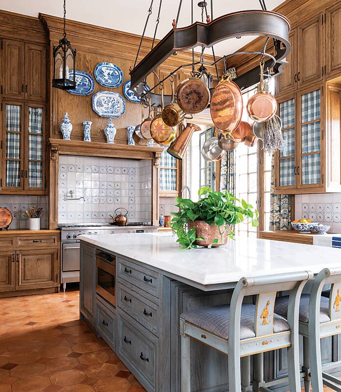 A kitchen with wood cabinetry, blue-and-white accents, and a pot rack hung with antique copper cookware