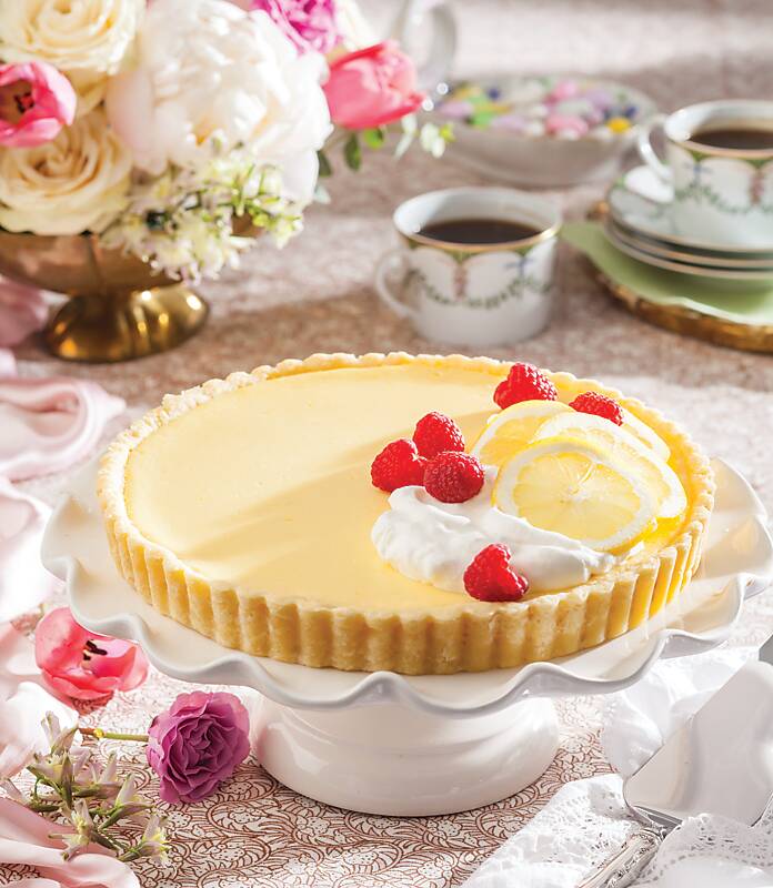 Lemon-Raspberry Tart served on a footed cake stand surrounded by pink and white flowers