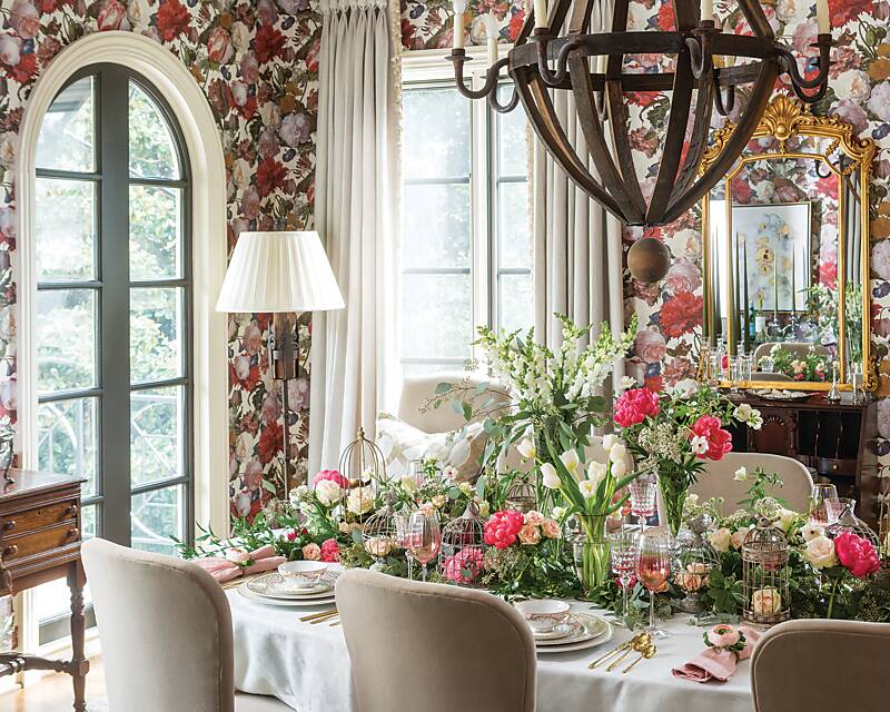 A dining room cloaked in floral wallpaper and a table set with abundant flower arrangements