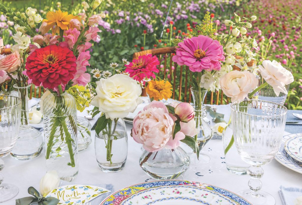 Pink and white flowers in clear bud vases on an outdoor tabletop