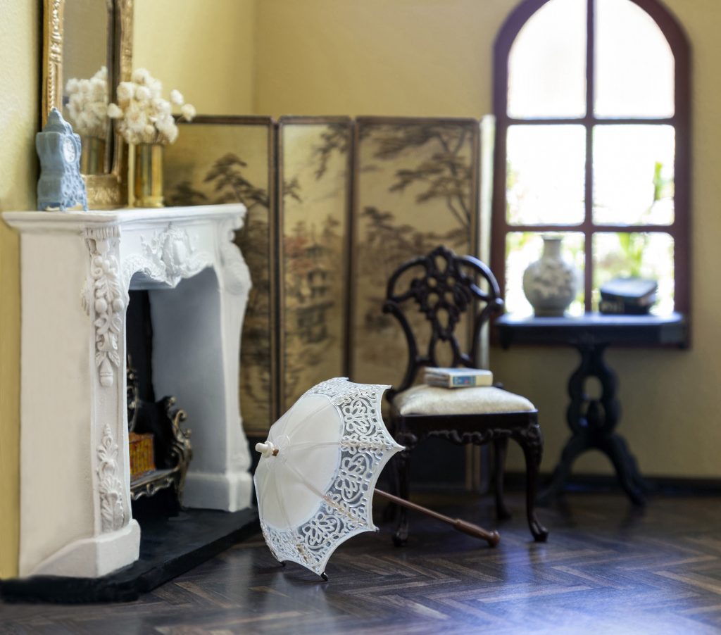 Room of a home with a single window, a white fireplace, and a lace umbrella
