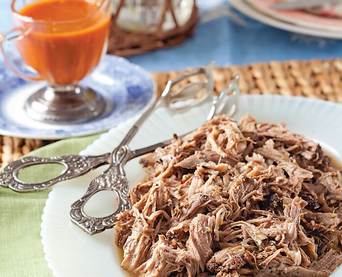Pulled pork on a white dish with silver tongs