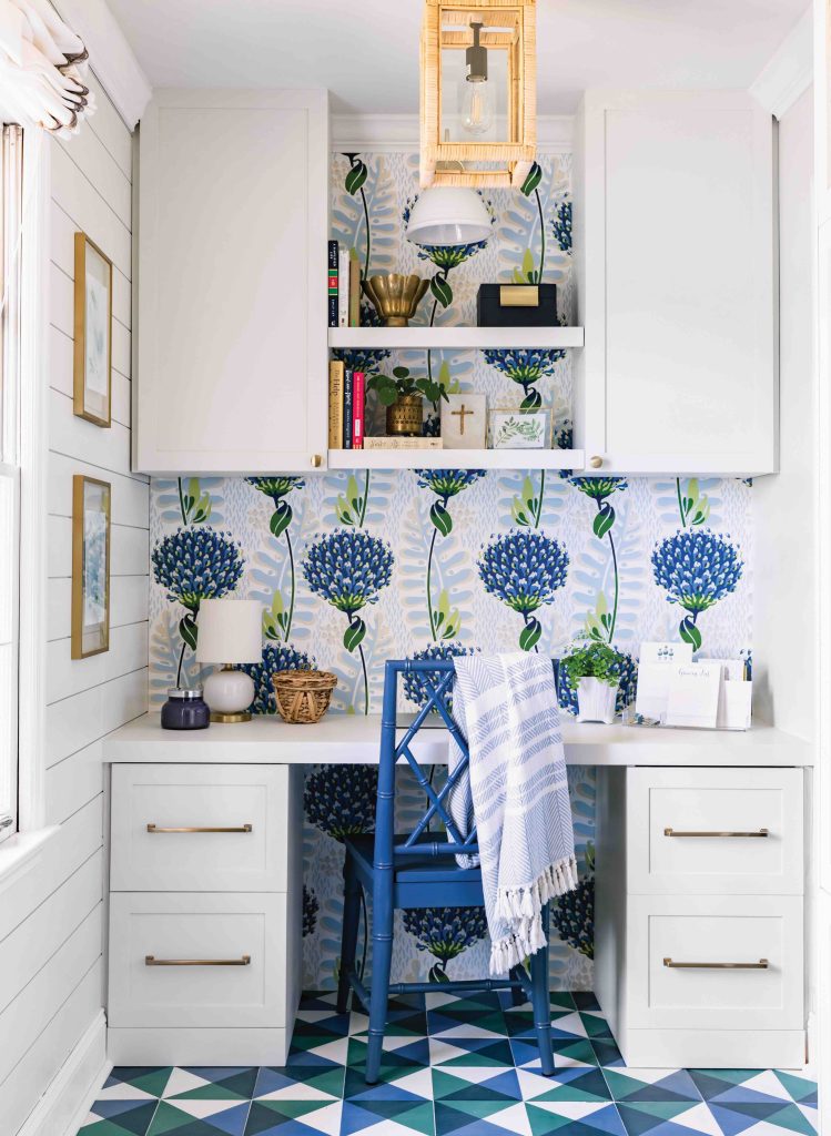 An office nook with a white built-in desk, blue floral wallpaper, and a geometric tile floor in shades of blue, green, and white