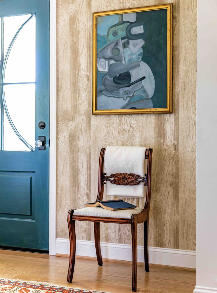 A foyer featuring faux bois wallpaper, a single antique chair, and a blue abstract painting