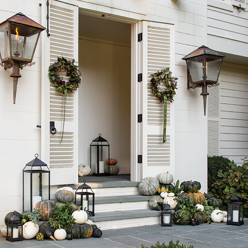 A whitewashed front porch featuring green and white pumpkins