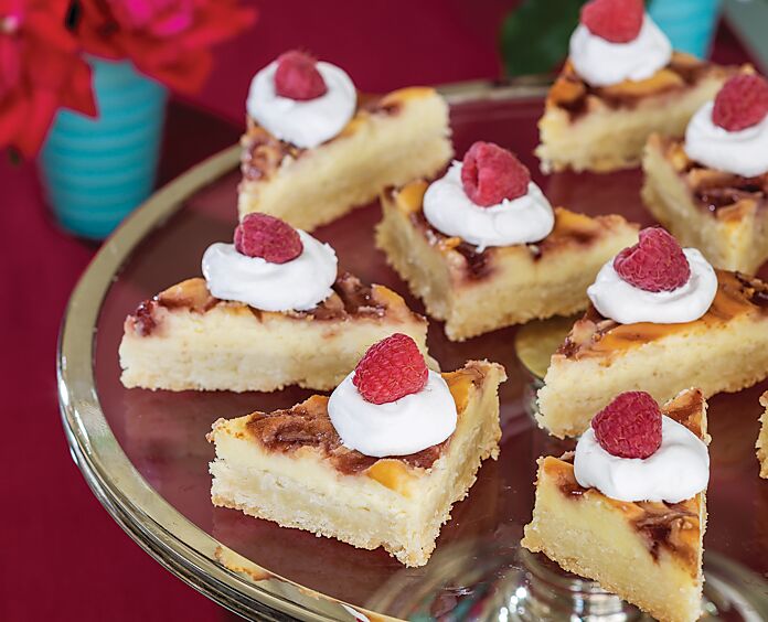 Cream Cheese Raspberry Coconut Bars on a silver-rimmed glass cake stand