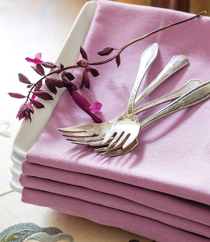 Stacked white plates covered with lavender linens and topped with three silver forks